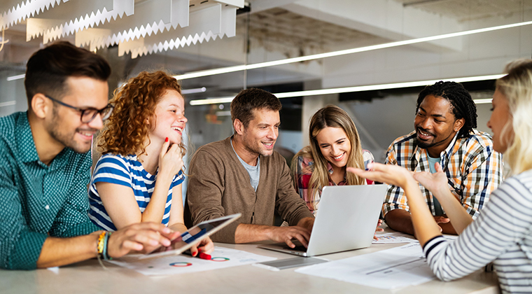 A group of coworkers sits around a computer discussing the benefits of a white label applicant tracking system. 