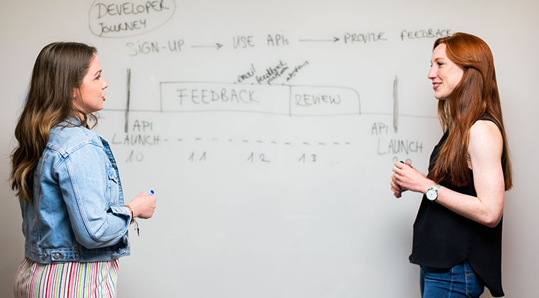 Two HRO professionals discuss how to increase revenue in front of a whiteboard. 