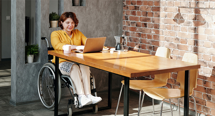 Young woman in wheelchair sitting at desk with open laptop