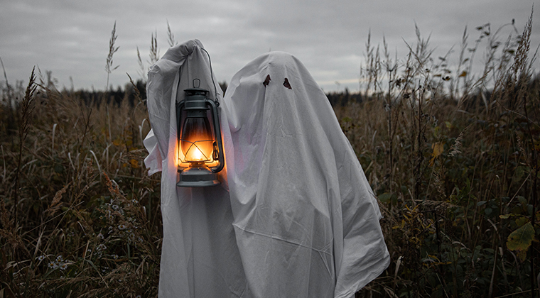 Person dressed as a ghost holding up a lantern