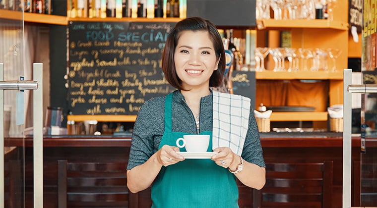 Smiling coffee shop waitress holding a cup of coffee.