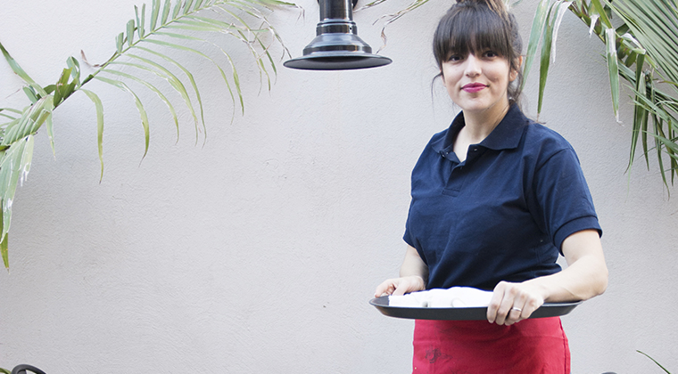 Female waitress standing outside a cafe holding a tray.