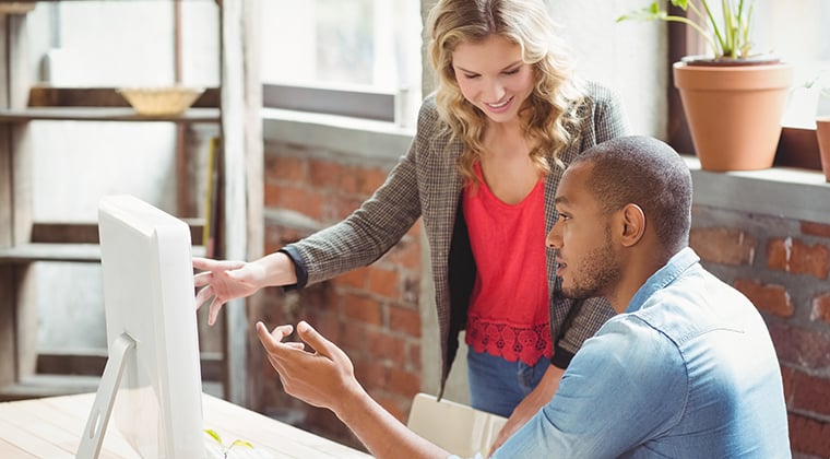 Two business people discuss recruiting software in front of a computer