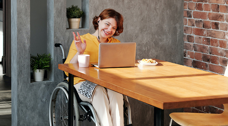 Young woman sitting in wheelchair in front of a table with an open laptop and cup of coffee.