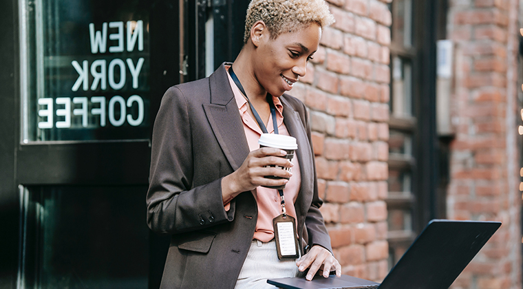 Woman working on laptop holding a coffee outside