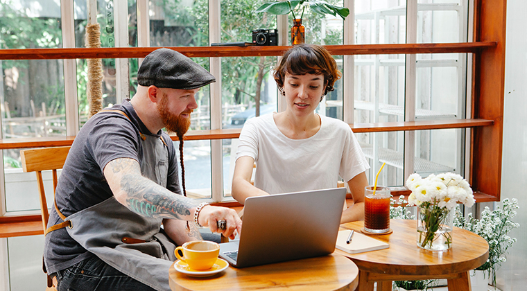 Two hospitality co-workers sitting down and looking at laptop in an outdoor patio.