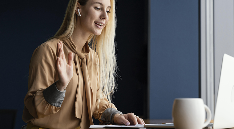 Side view of a woman waving while having a video conference call from laptop