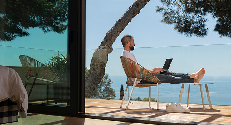 Man sitting on balcony with feet up and a laptop in his lap.